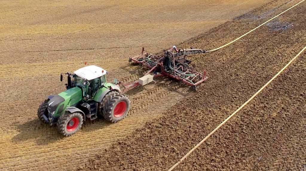 green tractor spreads biosolids in an open field