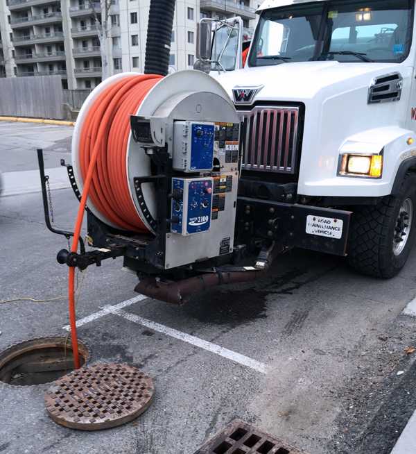 orange hose from a hose reel on the front of a large truck going into a manhole