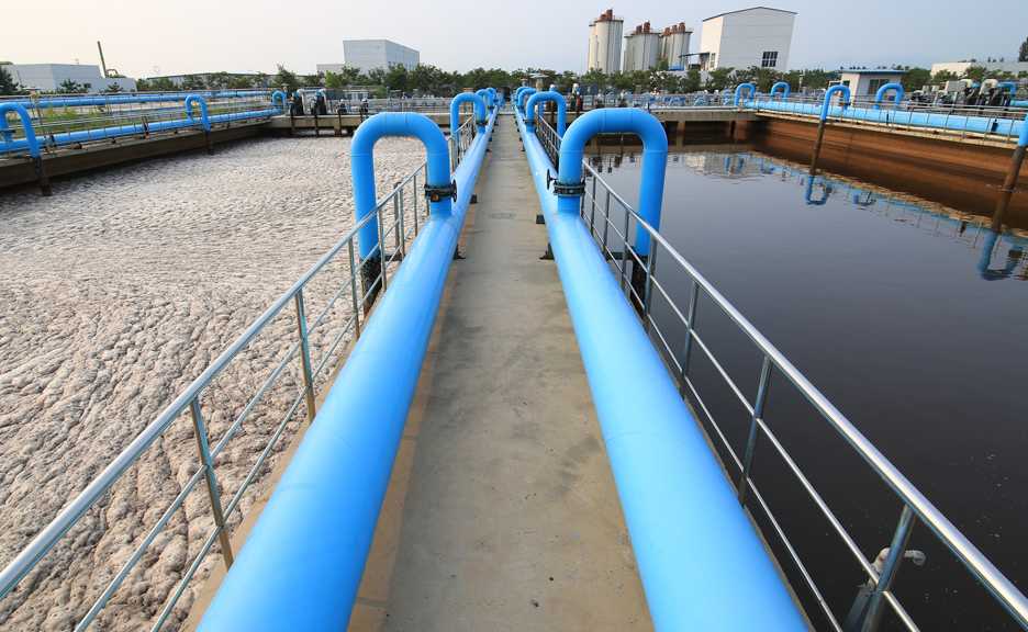 a walkway between two wastewater tanks with blue pipes running down the edges
